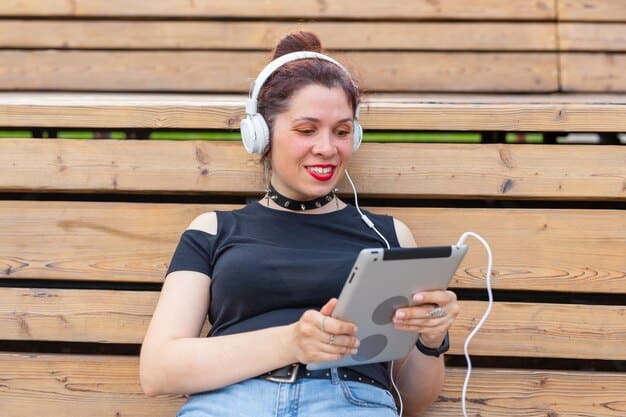 A person wearing headphones and smiling while listening to an audiobook on a tablet. The background shows a cozy living room, emphasizing the comfort and accessibility of consuming literature through streaming platforms.