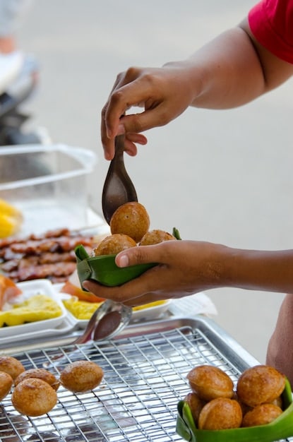 A close-up of steaming Acarajé being prepared by a traditionally dressed Bahian woman on a street in Salvador, Bahia. The scene captures the vibrant colors of her clothing, the bubbling oil in the pan, and the textures of the ingredients used.